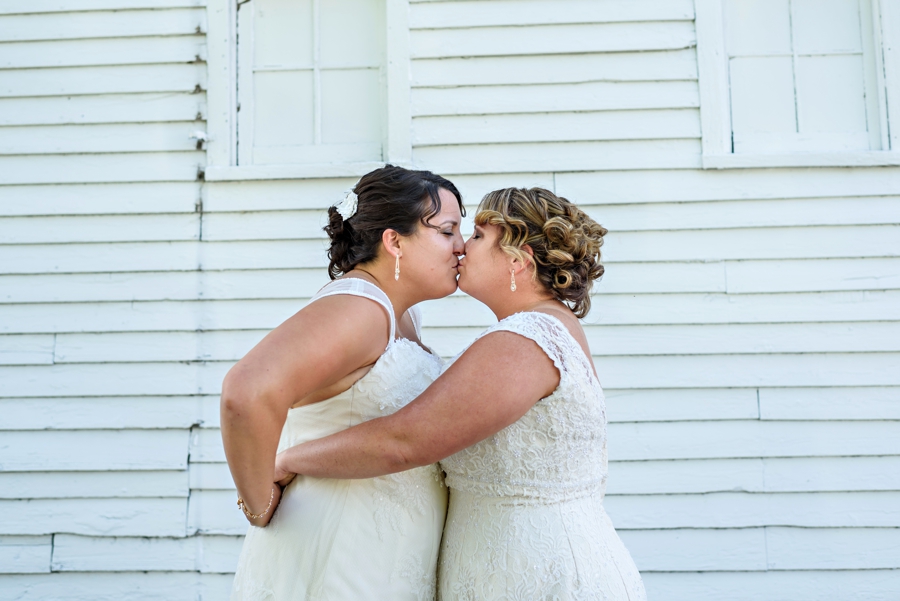Two brides kissing after seeing each other for the first time in their wedding dresses.
